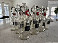 Set of 12 clear glass bottles with bale wire swing top closures and black chalkboard labels, arranged on a table.