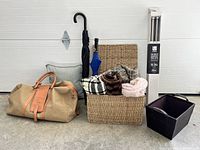 Full view of lot showing rattan basket with blankets, canvas tote, umbrellas, storage bin, and boxed drapery rod.