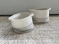 Two contemporary cream and grey rope storage baskets placed on a beige and cream chevron patterned carpet.