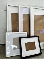 Six picture frames arranged against a wall showing various sizes and colors white and black with matting inside.