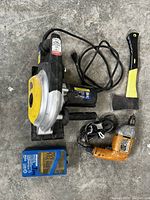 Full view of all items including Powerfist metal cutting saw, Black & Decker drill, hatchet, and blue Mastercraft drill bit case laid on concrete surface.
