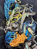 Top view of assortment including braided ropes in various colors, flat webbing straps, and metal ratchet straps inside black container.