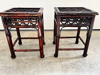 Front view of two smaller dark reddish wood side tables with black metal lattice top and decorative circular frame details