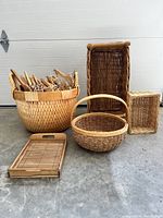 Photo showing the large round wicker basket filled with wooden coat hangers, tall rectangular wicker basket, smaller rectangular wicker basket, round wicker basket with handle, and wooden tray arranged on concrete floor.