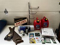 Photo showing entire lot on a white table against a white wall with all items clearly visible including jerry cans, tailgate seals, handsaws, hooks, small hardware packets, flexible vinyl duct, metal frame with hooks, and warning sign.