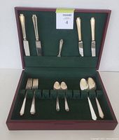 Photo of the 1847 Rogers Bros flatware set inside the open wooden storage case lined with green felt, showing knives, forks, spoons and butter utensil in their holders.