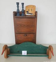 Front view of lot showing wooden vegetable storage bin, dark blue candlestick holders, loon light switch cover on top, and green wooden duck-head towel bar in front.
