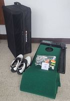 Photo showing black World of Golf car trunk organizer standing upright next to size 8 white and black golf shoes plus green putting system with accessories placed on top.