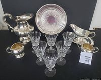 Full lot showing silverplate water jug, gravy boat and tray, cream and sugar bowl, and 6 crystal wine glasses arranged in front.