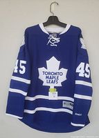 Front view of blue Toronto Maple Leafs hockey jersey with #45 and leaf logo, showing size tag and Reebok logo on sleeve.