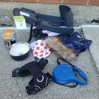 Photo of all lot items arranged on pavement including bicycle carrier seat, winter coat, bandanas, leash, harnesses, and bowl