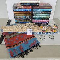 Photo showing stacked collection of 20 hardcover Jayne Ann Krentz books, folded cashmere pashmina shawl with multicolor pattern, two stemmed wine glasses decorated with fruit designs, and hammock ropes with wooden spreader bars arranged on flat surface.
