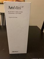 White product box of the AroMini BT Bluetooth Nebulizing Fragrance Diffuser by Aroma shown against a dark background.
