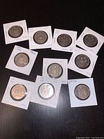 Eleven Canadian 50 cent coins from the 1970s housed in individual coin holders displayed on a black surface.