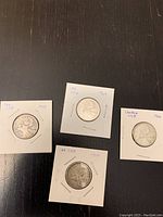 Photo showing four Canadian 25 cent silver coins individually mounted in white holders with handwritten dates 1943, 1960, 1964, and 1966, arranged on a dark surface.