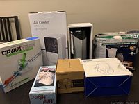 Lot of miscellaneous electronics showing boxed mini mixer, air cooler, thermaltake CPU cooler, wireless headphones, and light fixture box