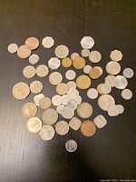 Photo of approximately 50 assorted foreign coins in different sizes, shapes, and metals placed on a black surface.