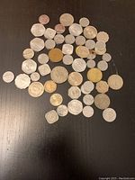 Photo of approximately 44 miscellaneous foreign coins on a dark surface showing different shapes, sizes and levels of wear.