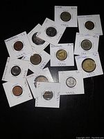Mixed assortment of 14 foreign coins from various countries and dates, in individual card holders showing years and some country labels.