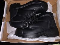 Pair of new black lace-up safety boots in a cardboard box with tissue paper, showing upper and side views.
