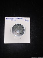 Obverse side of the ancient imperial coin showing weathered and worn details with the coin mounted in a white card holder.