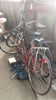Two bicycles parked side by side, red Capri bike in front and green cruiser bike behind with weights on floor