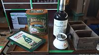 Photo showing Canadian Club bottle, Bailey's tin, Mountain Dew sign, white ceramic sugar bowl, and wooden ammunition box