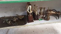 Brass tray with ornate bird candle holders, trophies, and teapot arranged on shelf.