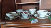 Set of five cups and saucers on wooden shelf, showing all cups together for overview.