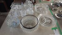 Overview of cut glass serveware items including bowls, baskets, decanters, and dishes with intricate cut glass patterns on a table.
