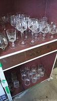 Two shelves of crystal cut glassware including wine glasses, tumblers, and brandy glasses.