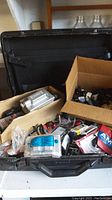 Wide view of black case filled with cardboard boxes containing various electrical parts, connectors, and accessories.