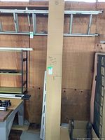 Wide view showing the long cardboard box against a pegboard wall, partially open with fluorescent tubes inside.