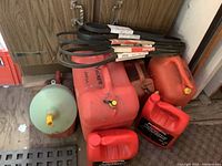 Three large red plastic gas cans with yellow caps, some visible wear. Automotive belts on top of cans.
