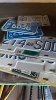Various British Columbia license plates in blue and white, showing multiple plates stacked including a white collector plate.