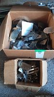 Box of assorted flat and angled metal plates with mounting holes in a large cardboard box