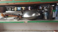 Overview photo showing pots, wok with lid, and double boiler (no lid) placed side by side on a shelf.