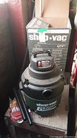 Shop-Vac 6.5 Gallon Wet/Dry Vacuum with box and two black extension tubes shown on wooden surface.