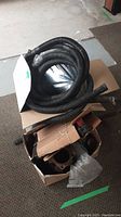 Coiled black flexible hose on top of a cardboard box with sump pump parts.