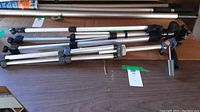 Photo displaying three tripods folded and laid horizontally on a wooden surface, showing leg details, locking clamps, and heads.