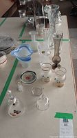 Photo showing assortment of glass vases and decorative glass pieces on a table, including blue Murano and tall bud vases