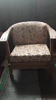 Front view of vintage wooden armchair showing floral upholstery and curved backrest.