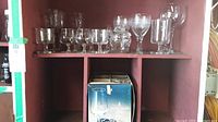 Wide view of shelf holding various glassware including a box of 6 red wine glasses and loose glasses above