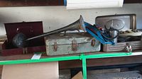 Overview of three vintage metal toolboxes and a metal horn laid out on a shelf showing varied signs of wear and rust.