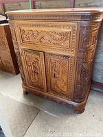 Front view of carved bar cabinet, showing ornate relief panels and curved corners