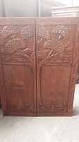 Front view of closed hinged carved wood doors showing landscape relief carving