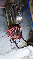 Top down view of the air compressor with coiled red hose and attached pressure gauge and spray gun.