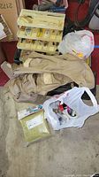 Lot overview showing beige fishing vest, multiple tackle boxes, fishing line package, and small fishing accessories in plastic bags.