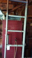 Full view of aluminum ladder leaning against a wall in a garage or shed, showing its length and condition with some dirt and stains.