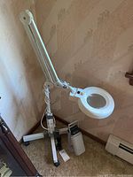 Full view of Ott Lite adjustable arm magnifier mounted on a rolling base with duct tape stabilizer, showing lens, articulated arm and power cord.